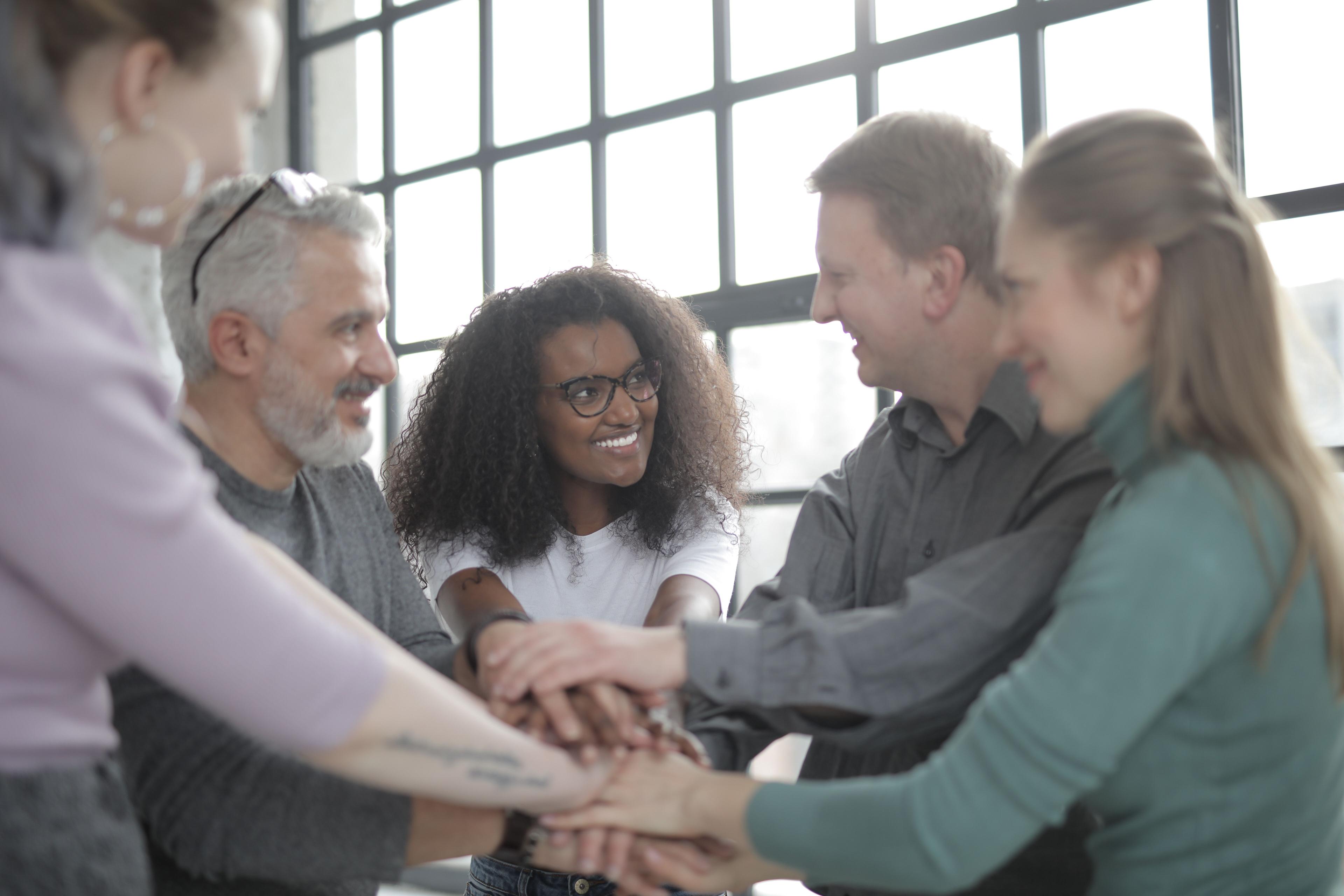 A team pulling together, clasping hands in the centre of a circle, denoting Nurture Cares values