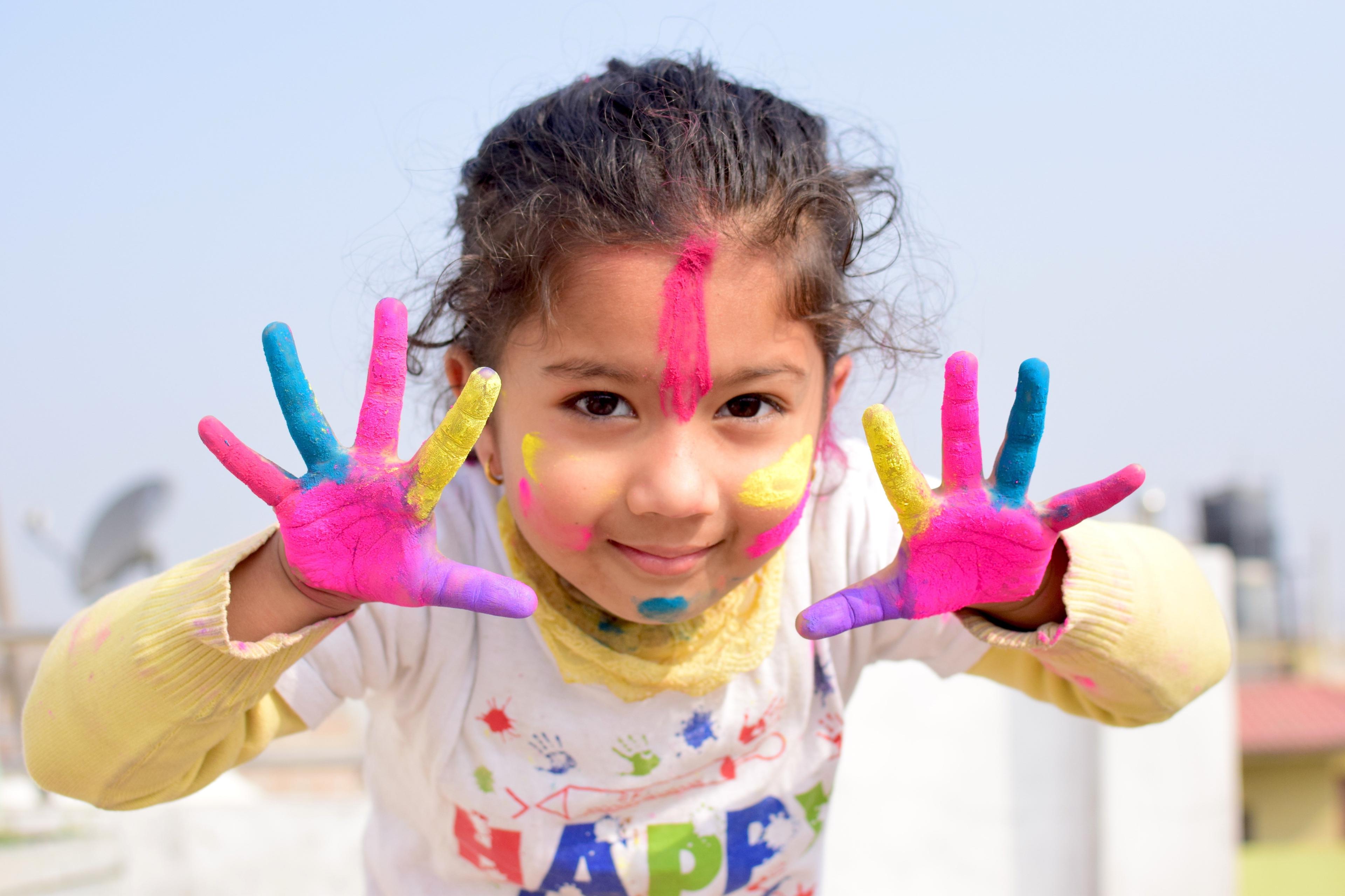 A bright happy girls with paint on her hands and face, denoting the child being central to everything Nurture Care does